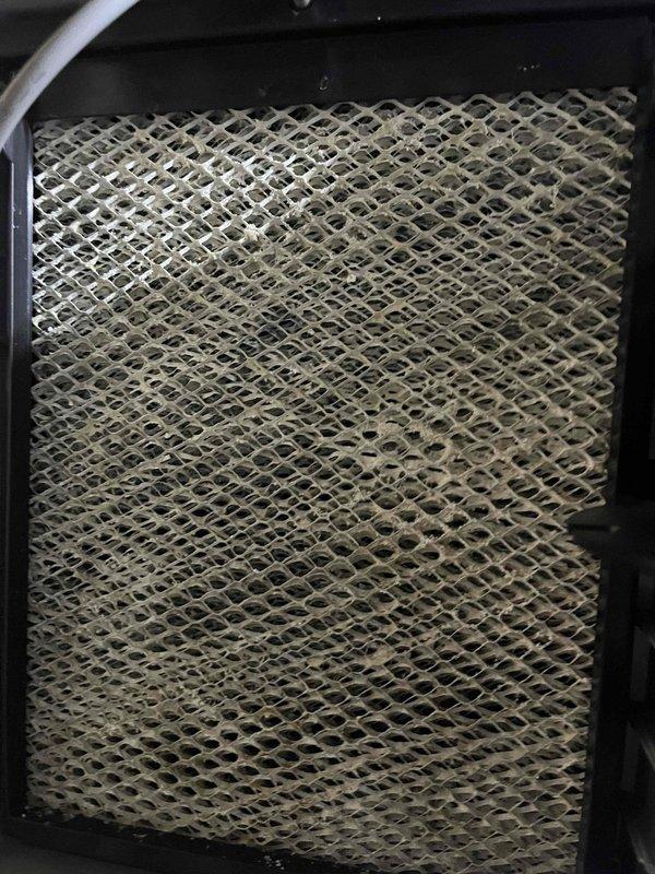 # HVAC Service - IAQ Report

Responded to service call for Aprilaire humidifier experiencing continuous water flow issue. Customer reported that humidifier pad required replacement and water was pouring through the unit, with flow persisting even after switching to summer mode, though at a reduced rate.

Upon inspection, found heavily discolored and mineral-encrusted humidifier pad with significant buildup throughout the mesh structure, indicating extended use beyond recommended service interval. The accumulation was restricting proper water distribution and drainage, causing water to overflow through the unit rather than evaporate normally. Replaced the saturated evaporator pad with new OEM filter media and verified proper installation within the black housing frame. Inspected the Aprilaire humidity control mounted on ductwork and confirmed settings were appropriate for seasonal operation. Tested water supply valve operation and drainage system to ensure proper flow control and verify