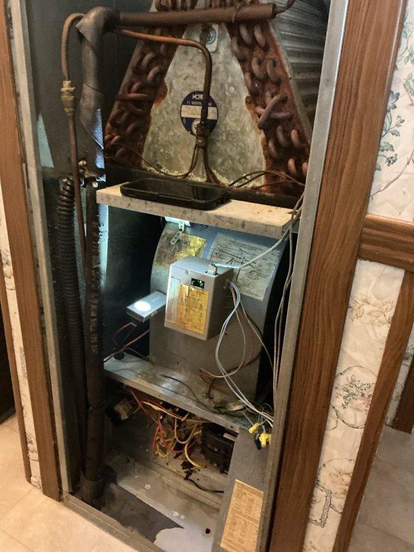 # Service Report: No Heat Call - Furnace Malfunction

Responded to a no heat service call for a 30-year-old Coleman furnace system that was continuously humming despite the thermostat being in the off position. Upon arrival, performed a comprehensive system inspection of the vertically-stacked HVAC installation housed in an interior closet space.

Visual inspection revealed extensive deterioration throughout the system. The evaporator coil exhibited severe rust and corrosion across the copper tubing and fin surfaces, indicating significant age-related degradation and possible refrigerant leakage. The coil assembly showed heavy brown oxidation that compromised its structural integrity and heat transfer efficiency.

Examined the air handler unit and identified the source of the continuous humming as a control board or blower motor malfunction preventing proper system shutdown. Traced electrical connections throughout the system, noting aged wiring and multiple connection points showing s