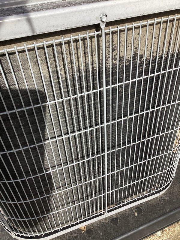 # Service Report: HVAC No Cooling Call

Responded to service call for 8-year-old Carrier system experiencing slow cooling with thermostat displaying service alert. Upon arrival, performed visual inspection of outdoor condenser unit and identified significant airflow restriction due to heavy accumulation of dirt, dust, and debris throughout aluminum cooling fin assembly. Debris buildup was particularly severe in lower portions of coil, with additional leaves, twigs, and organic matter collected on top protective grille and throughout unit exterior.

Performed thorough coil cleaning to restore proper airflow and heat transfer capacity. Removed protective grille to access condenser coil assembly. Cleared organic debris from top of unit and surrounding areas. Applied specialized coil cleaning solution and carefully cleaned cooling fins to remove embedded dirt and environmental contaminants without damaging delicate aluminum fin structure. Straightened any bent fins to maximize airflow effi