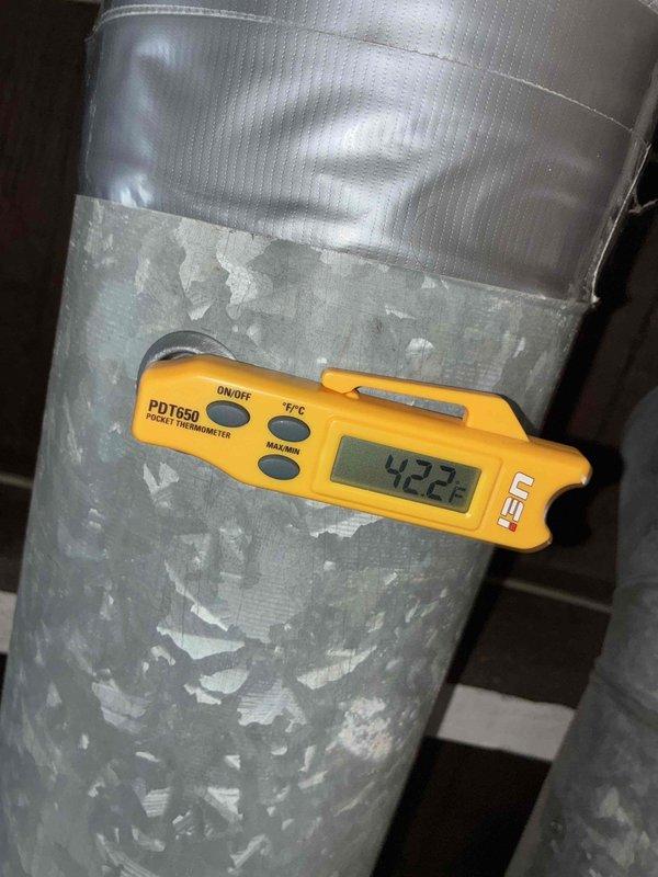 # Service Report: A/C System Performance Evaluation

Responded to service call for cooling system not maintaining set temperature on residential unit under 10 years old located in side yard. Upon arrival, performed comprehensive system diagnostics using digital manifold gauges to assess refrigerant pressures and system operation.

Conducted temperature measurements at supply ductwork, recording 42.2°F at the supply plenum, which falls within acceptable range for proper cooling operation. However, noted significant deterioration of duct insulation coating with peeling and flaking material on supply ductwork, which could contribute to reduced system efficiency and thermal loss. Flexible duct tape repairs visible on upper section of ductwork indicate previous maintenance attempts.

Connected professional diagnostic gauges to outdoor condensing unit to evaluate refrigerant charge levels, compressor performance, and overall system pressures. Unit installed on concrete pad with electrical se
