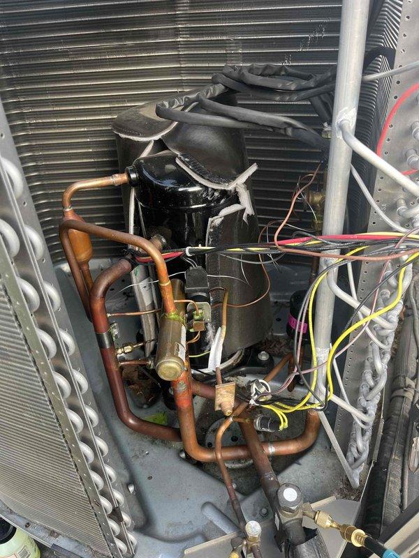 # Service Report: HVAC No Cooling Repair

Responded to service call for 9-year-old residential air conditioning system with no cooling condition and blinking red diagnostic light on outdoor unit. Upon arrival, performed visual inspection and diagnostic assessment of the condensing unit.

Removed outdoor unit access panel to inspect internal components and identify source of system failure. Located compressor assembly, refrigerant lines, condenser coil, and electrical connections. Observed blinking red diagnostic code indicating system fault condition.

During detailed inspection of refrigerant circuit, discovered significant deterioration and failure of copper suction line. Identified longitudinal split in copper tubing with visible corrosion, green patina from copper oxidation, and compromised pipe integrity. The damaged section exhibited brown discoloration and dark patches indicating advanced corrosion. This refrigerant line failure resulted in complete loss of refrigerant charge an