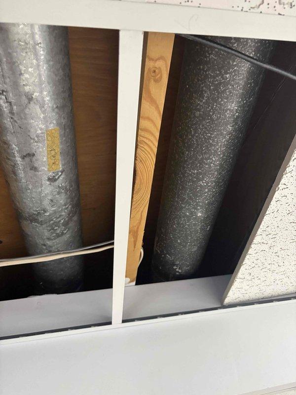 Responded to service call for noisy heating register with suspected loose component. Upon inspection of 14-year-old furnace system, examined ductwork and register connections in utility space. Identified source of noise originating from supply duct assembly near wooden framing members. Inspected metallic ductwork sections showing normal wear patterns and verified proper installation of all accessible components. Documented existing conditions with photographs showing duct configuration, structural mounting, and component placement. Coordinated service visit within customer's morning availability window to accommodate scheduling constraints. System operational upon completion of inspection.