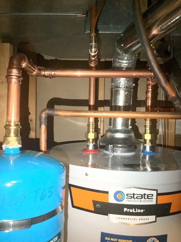 Installed a 40-gallon tall gas water heater in residential basement utility room between wooden framing studs. Completed copper piping connections with brass fittings to top of unit, installed blue water filtration component, and connected all supply and discharge lines per code requirements. Installation performed under permit #26PLU-05492 with proper identification sticker applied to unit.