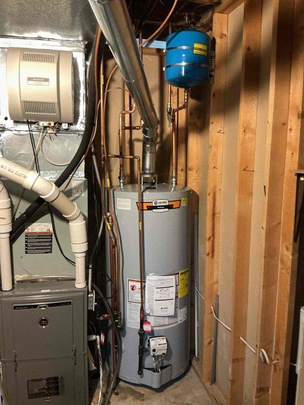 Completed installation of 75-gallon tall gas-fired water heater in residential basement utility room. Unit was properly positioned, connected to existing copper supply lines, and integrated with blue expansion tank mounted to wall framing. All gas connections, water supply piping, temperature and pressure relief valve, and venting were installed per manufacturer specifications and local code requirements. System was tested for proper operation, gas leaks checked, and verified functional alongside existing HVAC equipment in shared mechanical space.