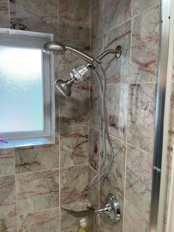 Completed plumbing repairs and upgrades in two bathrooms. In the hall bathroom, removed and secured loose shower valve assembly within wall cavity, patched wall openings, reinstalled and caulked tub spout, re-caulked toilet base seal, and upgraded 6-inch shower arm to 8-inch brushed nickel arm with escutcheon cover. In the master bathroom, replaced existing 6-inch shower arm with 8-inch brushed nickel arm and escutcheon cover. Performed leak testing on all repaired fixtures and connections in both bathrooms to verify proper installation and water-tight seals.