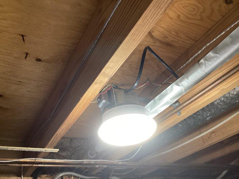 Completed comprehensive electrical inspection of residential property. Evaluated exposed basement ceiling infrastructure including lighting fixtures, electrical panel with dual-row circuit breaker configuration, and associated wiring systems. Documented condition of electrical panel showing multiple branch circuits with red, black, and white conductors, examined recessed LED lighting installation with visible mounting hardware and support conduit, and assessed overall electrical system integrity in unfinished utility space. Photographed findings for record-keeping purposes, noting exposed insulation material near electrical components and standard residential electrical installation configuration.