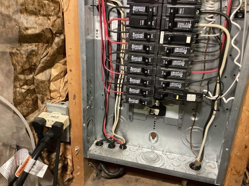 Completed comprehensive electrical inspection of residential property. Evaluated exposed basement ceiling infrastructure including lighting fixtures, electrical panel with dual-row circuit breaker configuration, and associated wiring systems. Documented condition of electrical panel showing multiple branch circuits with red, black, and white conductors, examined recessed LED lighting installation with visible mounting hardware and support conduit, and assessed overall electrical system integrity in unfinished utility space. Photographed findings for record-keeping purposes, noting exposed insulation material near electrical components and standard residential electrical installation configuration.