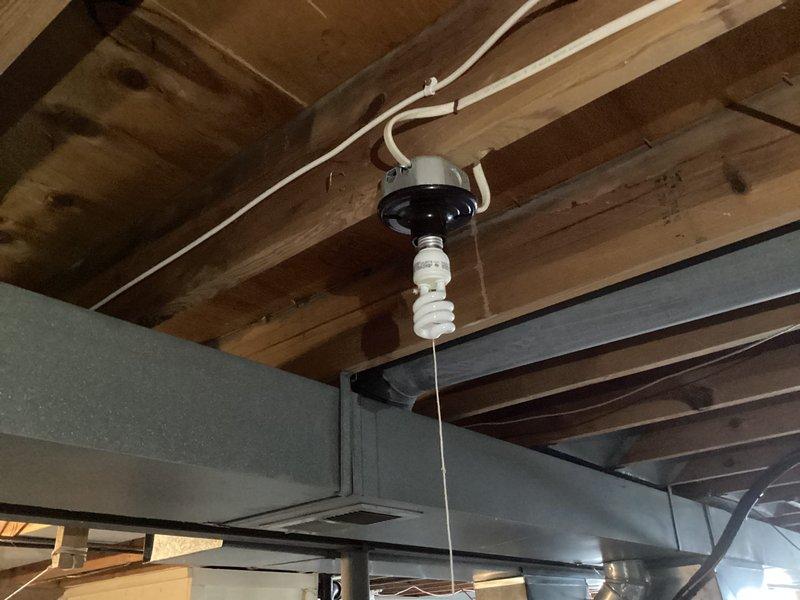 Completed comprehensive electrical maintenance home audit of unfinished utility space, inspecting exposed ceiling infrastructure including wooden joists, beams, and structural framing. Evaluated existing electrical systems including CFL lighting fixture with black circular mount, white electrical conduit routing and fastening methods along ceiling joists, and various electrical wiring running through framing members. Assessed HVAC ductwork positioning and metal support straps, verified proper clearances between electrical components and mechanical systems including gray rectangular ductwork and copper piping. Documented exposed infrastructure conditions, insulation placement between framing members, and overall electrical installation compliance with building codes. Photographed all findings for maintenance records.