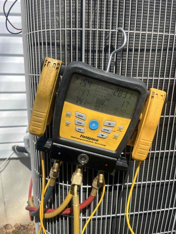 Responded to no cooling complaint on 15-year-old air conditioning system. Upon arrival, found unit running continuously but failing to produce cool air. Diagnostic testing with manifold gauges revealed abnormal temperature readings of 159°F and 147°F, indicating severely restricted airflow across the condenser coil. Inspection of outdoor unit uncovered significant blockage caused by bird nesting material lodged in and around the condenser coil fins and adjacent drainage piping. The accumulated debris consisting of twigs, straw, and dried plant matter was restricting proper heat exchange and preventing adequate refrigerant condensing. Removed all nesting material from condenser unit and surrounding area. Cleaned condenser coil fins to restore proper airflow. System tested after cleaning showed improved performance and proper cooling operation restored.