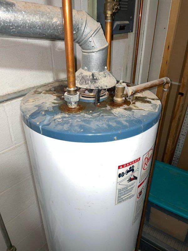 Responded to service call for thermostat displaying battery replacement error message on a 2-year-old system located in main floor hallway. Upon arrival, removed thermostat cover and inspected internal components, confirming unit does contain battery compartment with two AA batteries installed despite initial report. Verified wiring connections on circuit boards and checked battery contacts for proper seating. Also documented water heater in mechanical room showing signs of water staining and mineral deposits around top connections and piping, which may indicate separate plumbing concerns requiring attention.