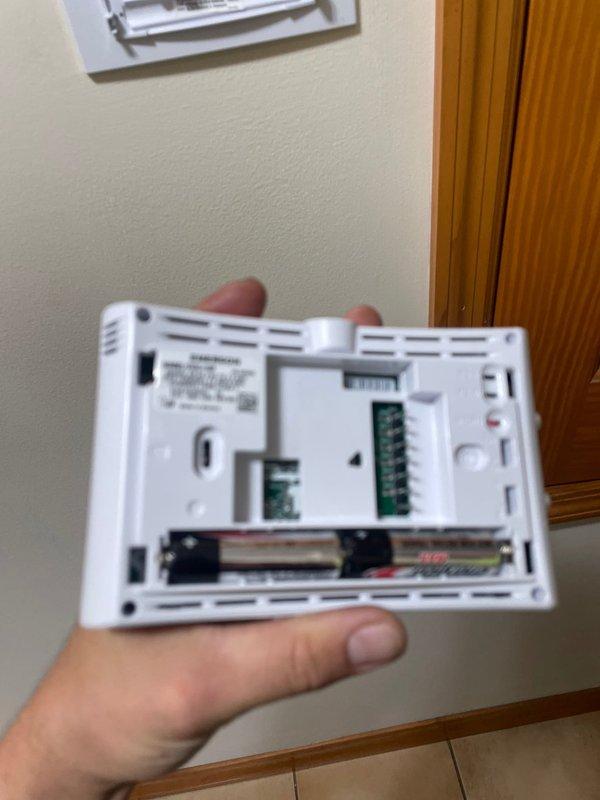 Responded to service call for thermostat displaying battery replacement error message on a 2-year-old system located in main floor hallway. Upon arrival, removed thermostat cover and inspected internal components, confirming unit does contain battery compartment with two AA batteries installed despite initial report. Verified wiring connections on circuit boards and checked battery contacts for proper seating. Also documented water heater in mechanical room showing signs of water staining and mineral deposits around top connections and piping, which may indicate separate plumbing concerns requiring attention.