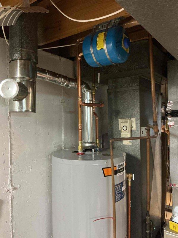 Completed installation of a 50-gallon tall gas water heater in basement utility area under permit 26PLU-06217. All copper supply lines, pressure relief valve, gas connections, and venting were properly installed per code requirements. Blue expansion tank was mounted to floor joists, all connections were tested for leaks, and plumbing identification sticker was affixed to the unit.