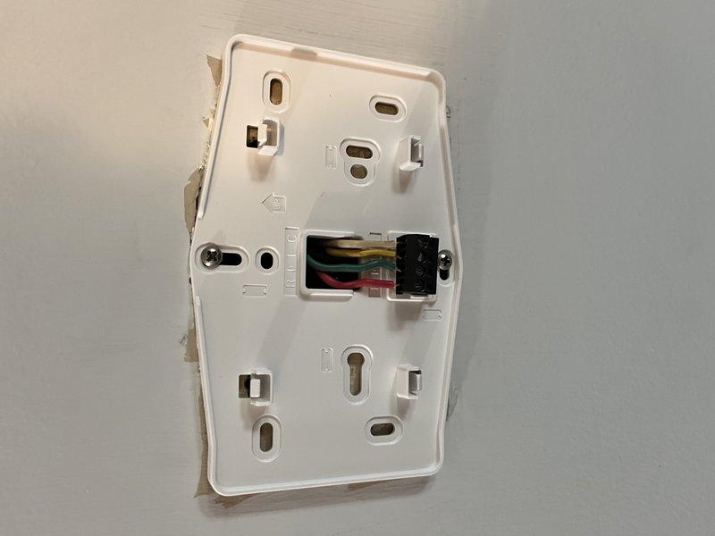 Responded to no-cool service call for 10-year-old Lennox system with unreadable thermostat display. Upon arrival, confirmed HVAC system was otherwise operational but thermostat screen was not functioning properly. Removed existing thermostat from wall and documented wiring configuration showing standard multi-conductor connections including R, Y, G, and C wires with wire nuts securing common connections. Diagnosed 11-year-old thermostat as failed unit beyond repair due to display malfunction. Removed defective thermostat and prepared wall plate for replacement installation. System restored to normal operation with readable display and full functionality.