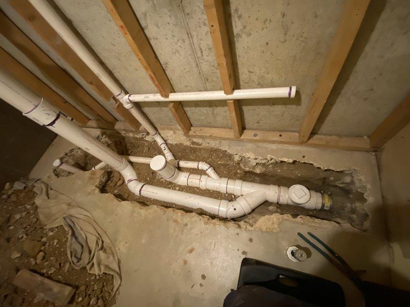 Completed plumbing rough-in installation for residential project including water supply lines and drainage system. Installed copper piping with brass fittings and water filtration component in upper level framing, along with PVC drainage assembly in lower level with proper venting and junction configurations. Performed water pressure testing to verify system integrity, followed by concrete patching of floor trenches where piping was installed. Retrieved testing equipment after successful inspection approval and completed final fixture installation including shower head in master bathroom.