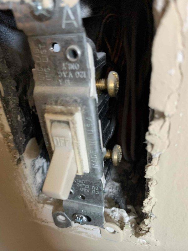 Completed comprehensive electrical safety inspection of residential property. Examined interior light switch installation, noting standard toggle switch with visible wear and dust accumulation around mounting box and exposed wiring connections. Inspected main electrical panel with cover removed, documenting circuit breaker arrangement, wire routing, and terminal connections on bus bars. All components photographed for record-keeping purposes. No immediate safety hazards identified during visual inspection.