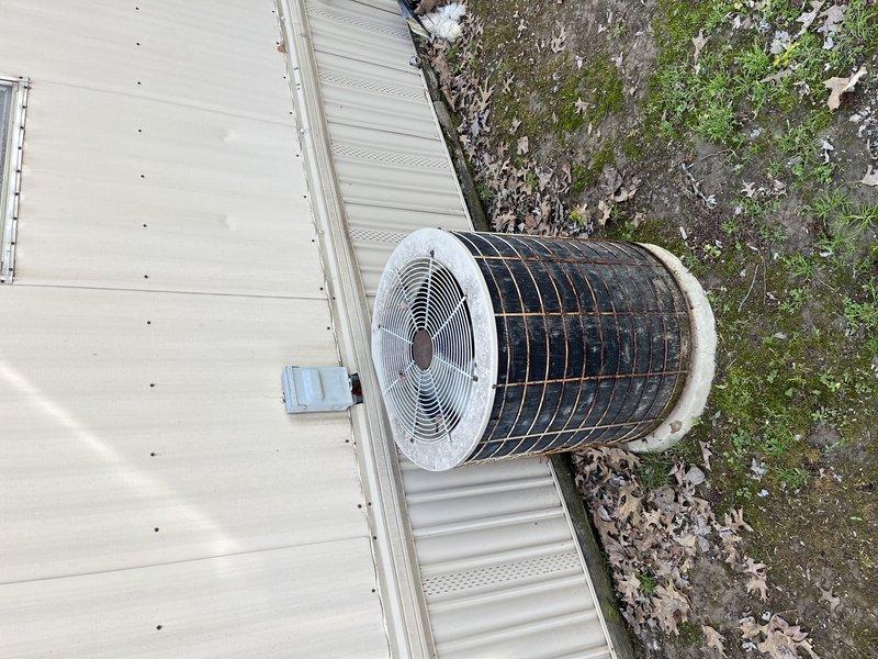 Responded to no cooling complaint on aging outdoor condenser unit located in side yard. Upon arrival, found unit with significant environmental wear, debris accumulation, and biological growth on surrounding surfaces. Performed diagnostic evaluation of system operation, inspected condenser coil condition through protective grille, and assessed electrical components including disconnect box. Documented equipment condition showing weathered exterior casing, darkened metal grating from oxidation, and dirt buildup affecting unit performance. Identified contributing factors to warm air discharge and provided recommendations for necessary repairs to restore proper cooling function.