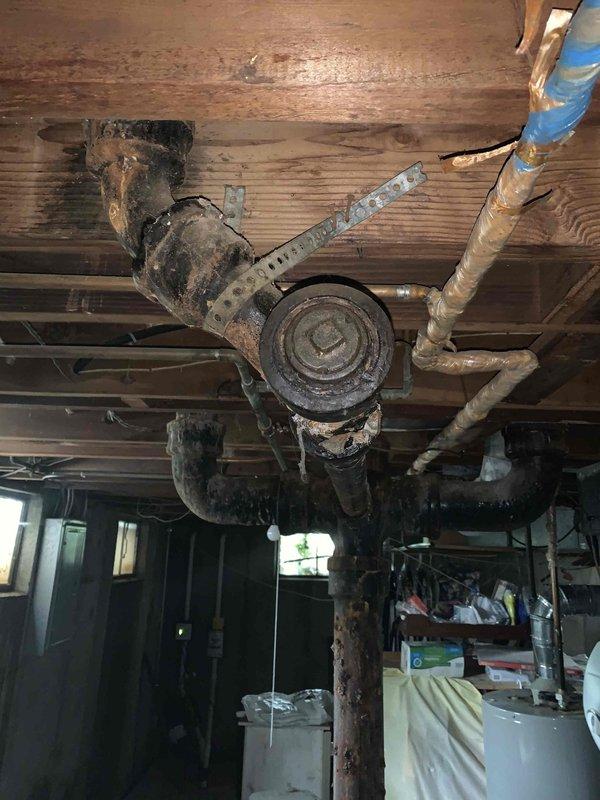 Responded to kitchen sink clog complaint and performed diagnostic inspection of drainage system. Upon investigation, accessed basement plumbing infrastructure and documented existing conditions of cast iron drain lines and associated piping components. Inspection revealed aging plumbing system with visible corrosion on cleanout fittings and drain assemblies beneath kitchen area. Assessed drainage configuration and confirmed presence of exterior sewer cleanout as reported. Photographed plumbing conditions including corroded cast iron piping, cleanout access points, and overall drainage layout for service records. Kitchen sink drainage issue addressed and system restored to proper working order.