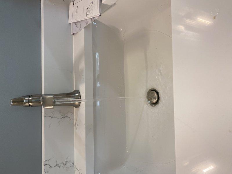 Completed trim-out installation of bathroom fixtures including shower assembly and lavatory plumbing. Installed chrome shower arm with mounting hardware and verified proper alignment and secure connection to supply lines. Connected P-trap assembly under vanity using PVC drainage components with threaded tailpiece, ensuring proper trap configuration and leak-free connections. Installed chrome shut-off valves for hot and cold water supply lines. All fixtures tested and verified operational with no leaks detected.