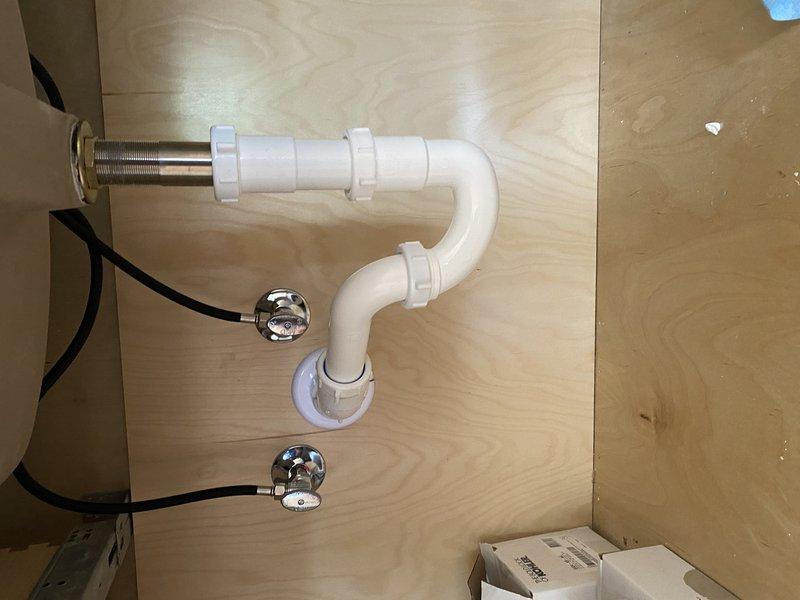 Completed trim-out installation of bathroom fixtures including shower assembly and lavatory plumbing. Installed chrome shower arm with mounting hardware and verified proper alignment and secure connection to supply lines. Connected P-trap assembly under vanity using PVC drainage components with threaded tailpiece, ensuring proper trap configuration and leak-free connections. Installed chrome shut-off valves for hot and cold water supply lines. All fixtures tested and verified operational with no leaks detected.