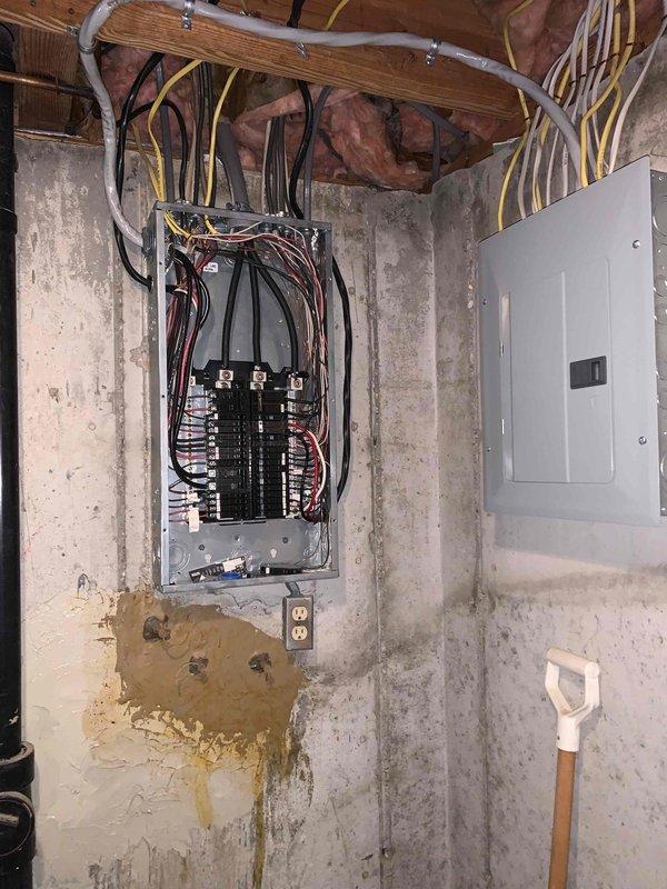 Completed comprehensive electrical inspection of residential basement utility area. Documented two electrical panels including one open panel revealing multiple circuit breakers with various amperage ratings (15A, 20A, 30A, and 100A main breakers), verified proper wire routing and connections, and noted presence of AFCI/GFCI breakers with blue test buttons in right column. Inspection revealed significant water staining on concrete block wall beneath left electrical panel indicating previous or ongoing moisture intrusion that requires monitoring for potential electrical safety concerns. Photographed exposed wiring, conduit routing including white PVC and yellow electrical cables, panel configuration, and overall condition of electrical infrastructure for documentation purposes.