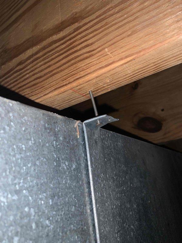 Responded to service call for loose ductwork in basement mechanical space. Upon inspection, found three sheet metal screws had backed out from galvanized duct hangers attached to floor joists, causing ductwork to separate from structural supports. Reinstalled and tightened all three mounting screws to secure metal ductwork brackets firmly to wooden framing members. Verified all connections were properly fastened and ductwork was adequately supported with no movement or gaps at attachment points. System returned to proper operational condition with all ductwork securely mounted to structural framing.