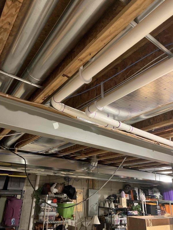 Removed existing PVC drain lines and water supply lines from original kitchen configuration. Re-routed 2-inch PVC drain piping and 1/2-inch water supply lines through basement ceiling joists to new island location, securing all lines per code requirements. Installed new loop vent system within the island hip wall to provide proper drainage venting for the relocated fixtures. Completed rough-in plumbing for kitchen sink drain and supply connections, dishwasher drain and supply hook-ups, and refrigerator water supply line at new designated locations. All piping installations positioned and ready for finish connections once cabinetry and appliances are set in place.