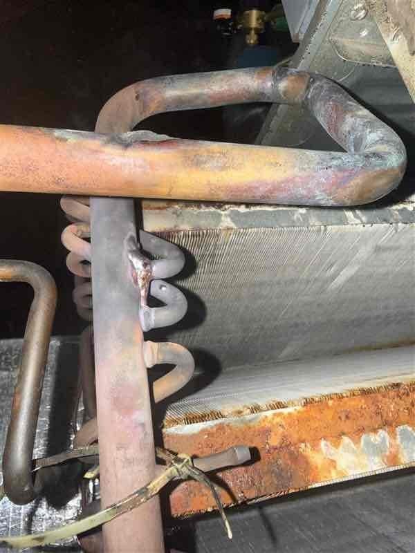 Responded to callback for evaporator coil leak repair on R22 system. Upon arrival, accessed attic-mounted air handler and located U-shaped copper refrigerant line exhibiting significant discoloration and oxidation indicative of leak point. Attempted leak repair per service manager authorization, however, extensive corrosion observed on lower heat exchanger section with heavy rust buildup on fins suggested systemic deterioration. Applied leak sealant to affected copper piping connections and monitored for stability. Recharged system with R22 refrigerant to manufacturer specifications. Documented existing conditions including corroded evaporator coil sections and compromised heat exchanger fins through photographic evidence for customer records and future service reference.