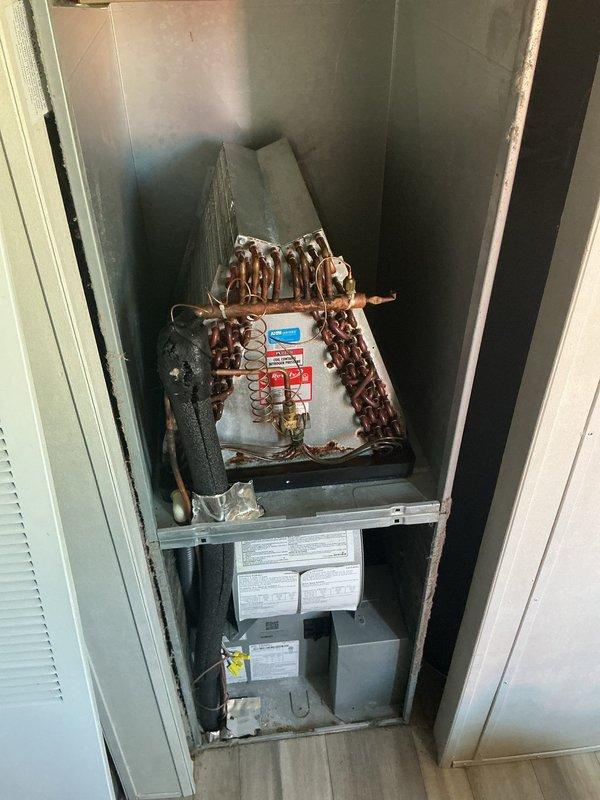 Responded to no-cool call on 4-year-old split system. Customer reported blower motor failure and frozen evaporator coil from previous night; unit had been turned off and allowed to thaw prior to arrival. Performed diagnostic testing on outdoor condensing unit using multimeter to check electrical components and compressor operation. Inspected indoor air handler and evaporator coil assembly located in laundry room closet. Verified blower motor functionality, checked refrigerant line connections, and tested system operation. Documented equipment condition with photos showing outdoor unit with test equipment connected and internal components of vertical air handler installation including evaporator coil and furnace assembly.