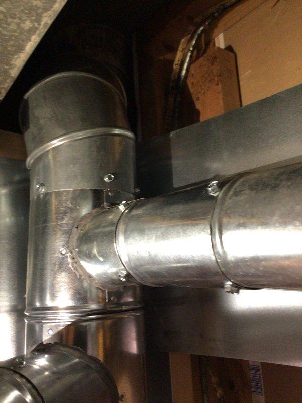 Responded to unit 10 basement for water heater exhaust connection. Inspected existing 5-inch galvanized vent pipe showing moderate rust staining and weathering at seams and joints. Connected exhaust ductwork to enable water heater installation, securing all connections with appropriate fasteners. Verified proper venting pathway through attic space with T-junction branch configuration. All metalwork secured and ready for water heater hookup.
