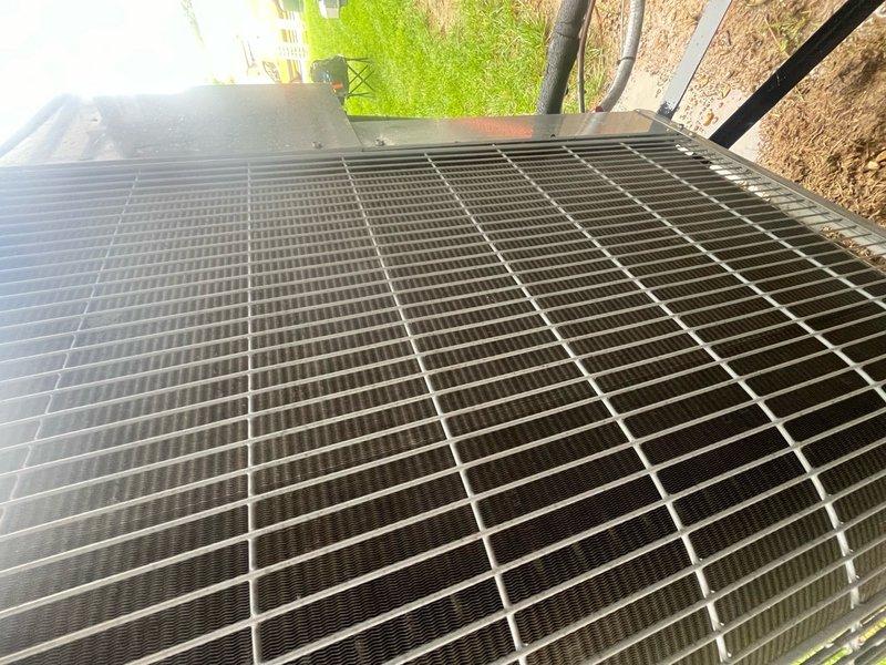 Completed comprehensive cooling system maintenance on single outdoor AC condenser unit. Performed standard tune-up procedures including inspection of protective grille, condenser coil, and external components. Unit found in operational condition with grille intact and coils accessible for service. Documented equipment condition through photographic records showing proper installation on grade-level pad adjacent to structure.
