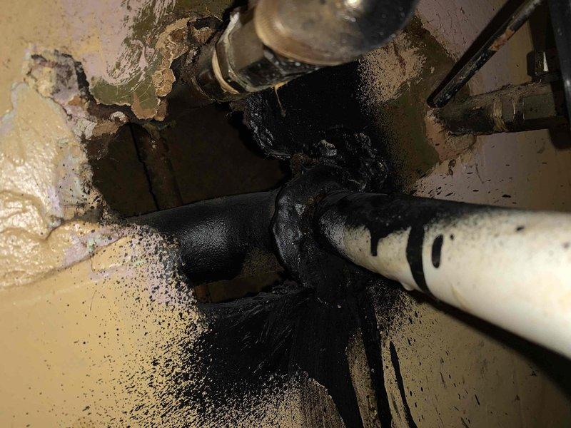 Responded to bathroom sink drainage issue and performed comprehensive assessment of plumbing system. Upon inspection, discovered clogged drain line was secondary to more significant underlying problems including active pipe leakage, severe corrosion on metal fittings and connections, and extensive water damage throughout the area. 

Documented deteriorated plumbing components with thick black viscous substance leaking from connection points, creating substantial staining on surrounding surfaces. White PVC piping showed age-related wear while metallic pipes displayed advanced corrosion, rust staining, and mineral deposit buildup. Multiple pipe connections exhibited signs of failure with ongoing leakage evident from fresh wet areas and drip patterns.

Found standing water accumulation on floor with biological growth including dark green and black mold/mildew covering multiple surfaces. Wall surfaces showed extensive deterioration with peeling paint, exposed substrate, and large sections 