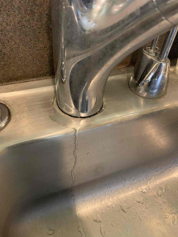 Responded to service call for dripping kitchen sink and slow-draining bathroom shower. Upon inspection, discovered significant vertical crack in kitchen sink basin extending from faucet base toward drain area, which was the source of the water leakage. Assessed bathroom shower drain and found metal drain cover with visible buildup and discoloration around perforations, restricting water flow. Documented both issues with photographs for repair recommendations. Customer advised that kitchen sink requires replacement due to structural damage and bathroom drain requires clearing and cleaning to restore proper drainage function.