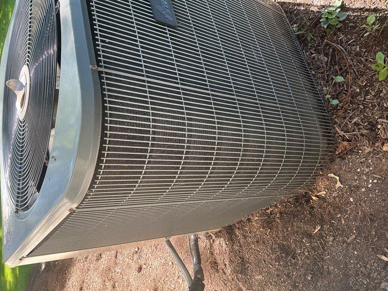 Completed cooling maintenance tune-up on outdoor air conditioning unit. Inspected cylindrical condenser coil with horizontal fins, verified proper operation of fan assembly and protective grille, and examined air filter with diamond-pattern mesh design. System confirmed operational with all components functioning within normal parameters.