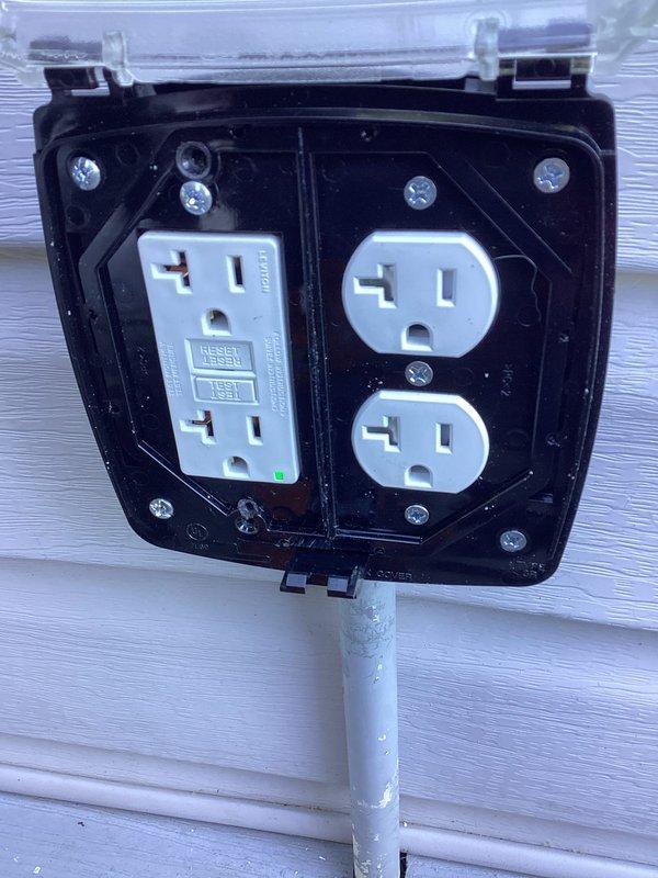 Replaced exterior deck outlet assembly with new weatherproof GFCI-protected configuration featuring four outlets in a black enclosure with clear protective cover and white conduit. Installation includes dual-section setup with GFCI outlet on left side and standard duplex outlet on right side, all properly grounded and secured to building exterior siding.