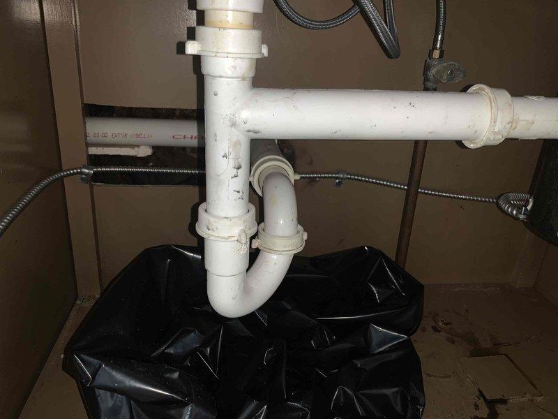 Responded to service call for kitchen double sink with drainage issue on garbage disposal side. Upon inspection, found existing garbage disposal unit contributing to clogging problem. Assessed under-sink plumbing configuration including white PVC P-trap assembly and drainage connections. Evaluated garbage disposal unit condition and drainage system functionality. Documented existing plumbing setup showing standard residential sink drainage with P-trap configuration, braided supply lines, and black cylindrical disposal unit with visible age-related wear. Prepared work area with protective measures to contain potential water spillage during service. Provided customer with assessment findings and replacement recommendations for garbage disposal unit to resolve ongoing drainage concerns.