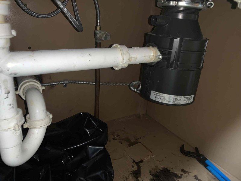 Responded to service call for kitchen double sink with drainage issue on garbage disposal side. Upon inspection, found existing garbage disposal unit contributing to clogging problem. Assessed under-sink plumbing configuration including white PVC P-trap assembly and drainage connections. Evaluated garbage disposal unit condition and drainage system functionality. Documented existing plumbing setup showing standard residential sink drainage with P-trap configuration, braided supply lines, and black cylindrical disposal unit with visible age-related wear. Prepared work area with protective measures to contain potential water spillage during service. Provided customer with assessment findings and replacement recommendations for garbage disposal unit to resolve ongoing drainage concerns.