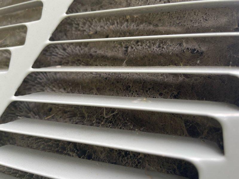 Completed AC tune-up on single ground-level unit located in garage area. Inspected and replaced heavily soiled return air filter showing significant dust and debris accumulation. Cleaned return air grille which exhibited substantial buildup of dirt, dust, and fibrous material behind louvers, restricting proper airflow to system.