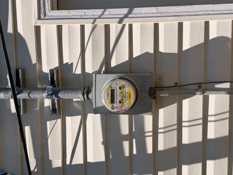 Responded to service call for exterior electrical panel that had become detached from building structure. Upon arrival, inspected meter enclosure and conduit mounting system on exterior wall with vertical siding. Repositioned and securely reattached the electrical panel enclosure to ensure proper mounting and safe connection to the home's exterior wall, verifying all conduit connections and hardware were properly fastened and meeting code requirements.