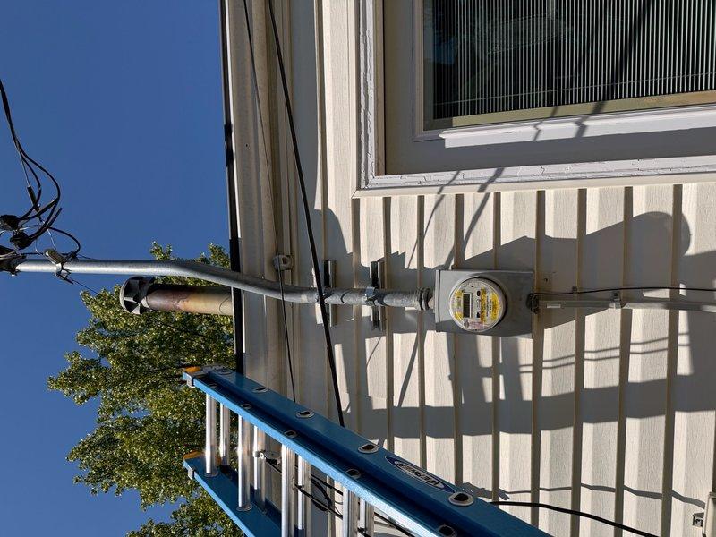 Responded to service call for exterior electrical panel that had become detached from building structure. Upon arrival, inspected meter enclosure and conduit mounting system on exterior wall with vertical siding. Repositioned and securely reattached the electrical panel enclosure to ensure proper mounting and safe connection to the home's exterior wall, verifying all conduit connections and hardware were properly fastened and meeting code requirements.