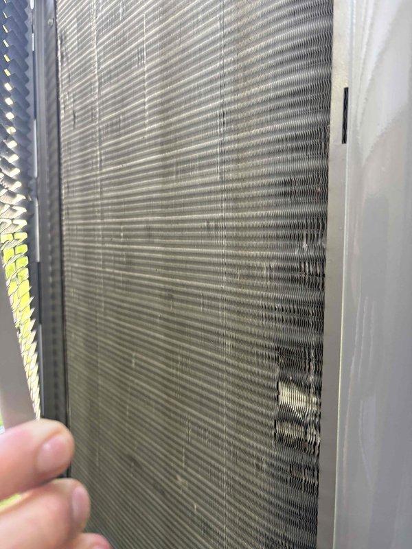 # Summary

Completed preventative maintenance tune-up on a 2012 single-stage air conditioning system, identifying damaged condenser coil fins that may impact heat transfer efficiency but unit remains operational.

# Work Performed

Performed comprehensive cooling season tune-up on outdoor condensing unit. Conducted visual inspection of all accessible components including condenser coil, control boards, and electrical connections. 

Inspected condenser coil and documented moderate fin damage in lower right section where aluminum fins are bent and compressed, reducing airflow through approximately 15-20% of coil surface area. Damage pattern suggests impact from lawn equipment or debris. Remaining coil sections maintain proper fin spacing and appear relatively clean.

Examined control board compartment and verified all electrical connections are secure. Multiple circuit boards with control modules show no signs of overheating, corrosion, or component failure. Wiring harnesses properly rou