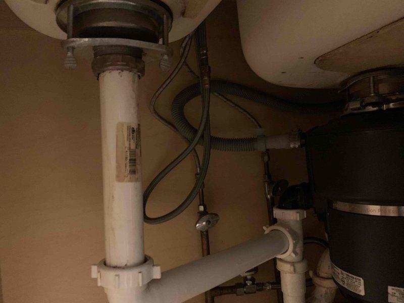 # Plumbing Service Completed

Responded to a kitchen sink drain obstruction in a 60-year-old residential property. Upon arrival, found that a component of the sink drain assembly had broken off, and a plumbing snake had been inserted into the drain line but became lodged and irretrievable deep within the piping system.

Inspected the under-sink plumbing configuration, which included white PVC P-trap assembly, water filtration canister, and standard drain connections. Assessed the stuck snake location and determined extraction methods. Due to the age of the home's plumbing system and the depth at which the snake was lodged, disassembly of drain components was necessary to access and remove the obstruction.

Removed the broken sink drain component and successfully extracted the lodged plumbing snake from the drain line. Cleared any remaining debris and blockage from the affected piping. Reassembled the drain system with proper connections, ensuring all PVC joints were secure and leak-fre