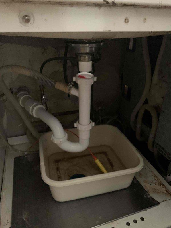 Responded to kitchen sink backup issue. Upon arrival, accessed cabinet beneath kitchen sink and inspected drainage system. Found P-trap assembly and connections associated with garbage disposal unit. Disassembled P-trap to clear blockage causing backup condition. Positioned collection basin to contain water and debris during service. Cleared obstruction from drain line, reassembled P-trap connections, and verified proper drainage flow restored to kitchen sink.