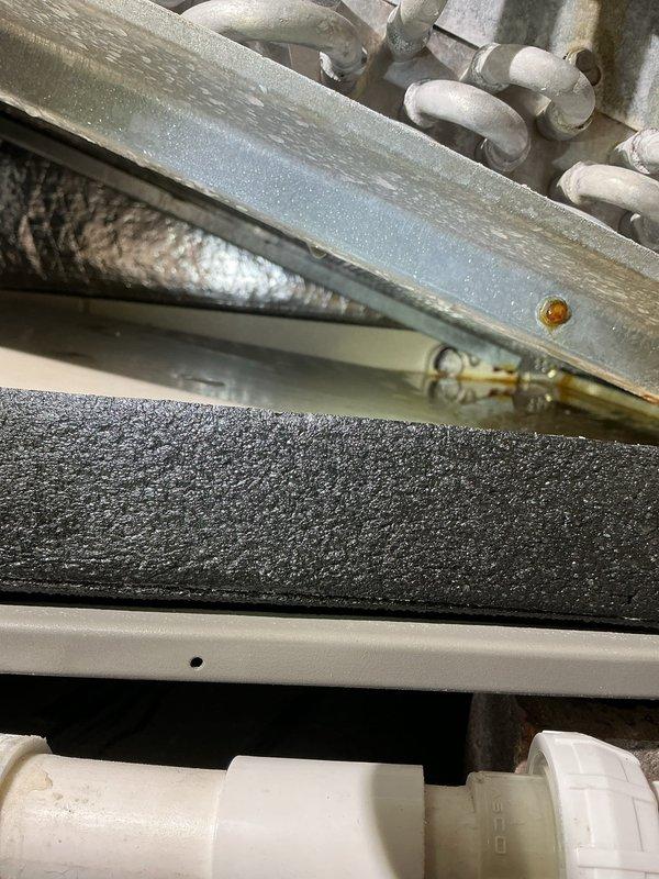 Responded to callback for HVAC system continuing to leak after previous repair. Accessed unit in attic and inspected condensate drain system and evaporator coil assembly. Upon examination, identified improper drainage from primary drain line and inspected drain pan for cracks or overflow conditions. Evaluated PVC drain piping configuration and brass fittings for proper connections and flow. Checked insulated refrigerant lines and surrounding areas for moisture accumulation. Documented current condition of drain pan, piping connections, and ductwork installation with photos showing metal drain pan assembly, PVC drain components, and flexible ductwork in attic space. Further diagnostic work required to identify source of persistent leak and implement permanent solution.