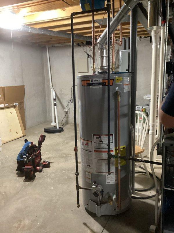 Completed installation of a 50-gallon gas tall water heater (State ProLine model) in residential basement. Connected all copper supply and discharge piping with appropriate brass fittings, installed gas line connections, and verified proper venting configuration. Unit was set up and prepared for delivery with all plumbing connections completed to code specifications.