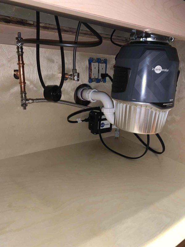 Completed finish plumbing installation for kitchen sink and dishwasher connections, including final hookup of water supply lines, drain assemblies, and water treatment system. Installed InSinkErator water filtration unit with copper supply piping, blue-handled shutoff valves, and white PVC drainage system with P-trap configuration, ensuring all connections were properly secured and tested for leaks.