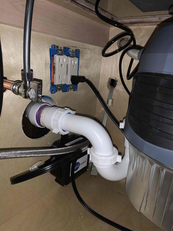 Completed finish plumbing installation for kitchen sink and dishwasher connections, including final hookup of water supply lines, drain assemblies, and water treatment system. Installed InSinkErator water filtration unit with copper supply piping, blue-handled shutoff valves, and white PVC drainage system with P-trap configuration, ensuring all connections were properly secured and tested for leaks.
