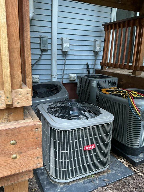 Responded to service call for tilting condenser unit at rear of property. Upon inspection, found Unit 10 condenser experiencing structural instability due to deteriorated pad support and settled deck foundation. Evaluated multiple outdoor condensing units positioned on wooden deck surface. Assessed compromised mounting surface and verified unit remained operational with no refrigerant leak detected. Documented existing conditions including weathered decking, proper electrical connections, and condensate drainage configuration. Recommended foundation reinforcement and pad replacement to prevent further tilting and potential refrigerant line damage.