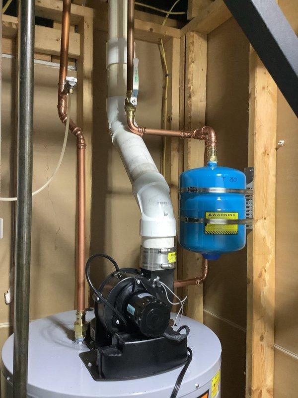 Installed 50-gallon power vent water heater with complete plumbing connections in residential utility space. Installation included mounting black power vent motor assembly on tank top, connecting copper supply and distribution piping with brass fittings, installing white PVC vent piping with proper elbow configuration, and integrating blue pressure expansion tank into the system. All copper piping, pressure connections, and electrical components were properly secured within the exposed stud wall cavity to code specifications.