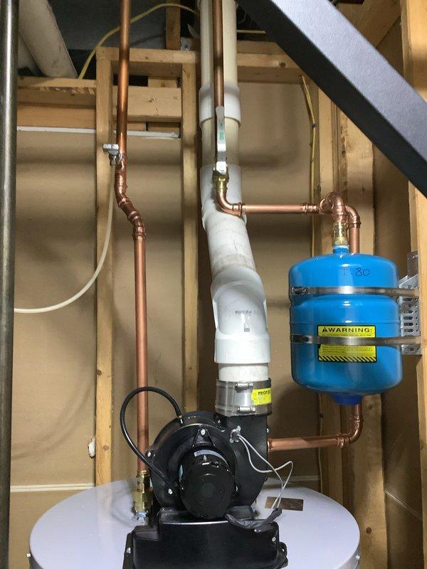Installed 50-gallon power vent water heater with complete plumbing connections in residential utility space. Installation included mounting black power vent motor assembly on tank top, connecting copper supply and distribution piping with brass fittings, installing white PVC vent piping with proper elbow configuration, and integrating blue pressure expansion tank into the system. All copper piping, pressure connections, and electrical components were properly secured within the exposed stud wall cavity to code specifications.