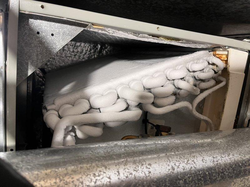 Responded to no cooling call on residential HVAC system that failed to operate after exterior unit was hosed off. Upon arrival, found evaporator coil completely encased in heavy frost and ice buildup, indicating restricted airflow or refrigerant issue. System was non-operational due to frozen coil condition. Documented equipment information and coil condition with photographs. Shut down system to allow coil to thaw completely. Diagnosed cause of freeze-up as likely related to restricted airflow from dirty filter, low refrigerant charge, or blower motor failure. Explained to customer that hosing off outdoor unit may have coincided with existing problem becoming apparent. Recommended allowing minimum 2-3 hours for complete defrost before further diagnostics could be performed to identify root cause and determine necessary repairs.